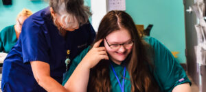 Female instructor overlooking female student's shoulder, both looking at something unseen in picture